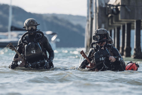 Navy SEALs emerge from the ocean on a beach.