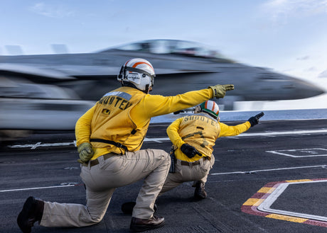 Sailors launch a fighter off a deck of an aircraft carrier.