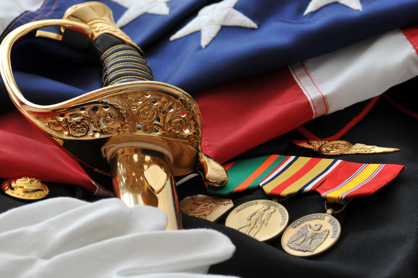 Decorative arrangement with a sword, medals, and an American flag on a dark surface.
