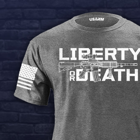 Gray t-shirt with 'Liberty or Death' graphic and USAMM logo on a dark brick wall background